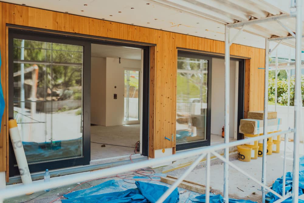 Pose de grandes baies vitrées coulissantes en PVC anthracite sur une façade en bois moderne.