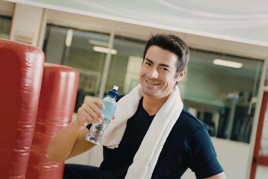 Un homme souriant dans une salle de sport tient une bouteille fraîche obtenue par vortex eau.