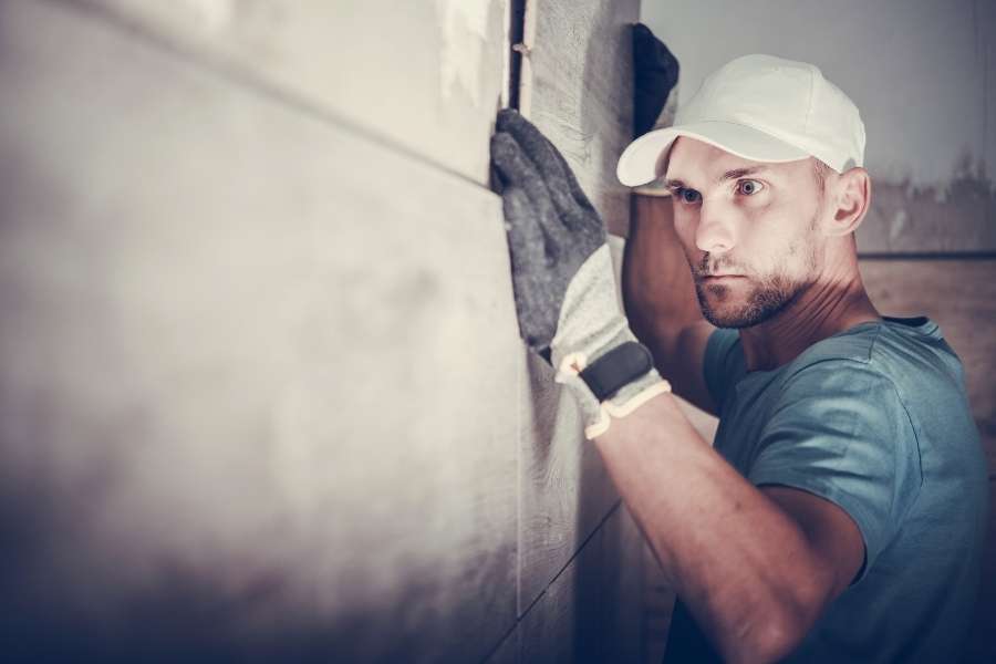 Un artisan concentré effectuant la pose du carrelage mural avec précision sur un chantier.