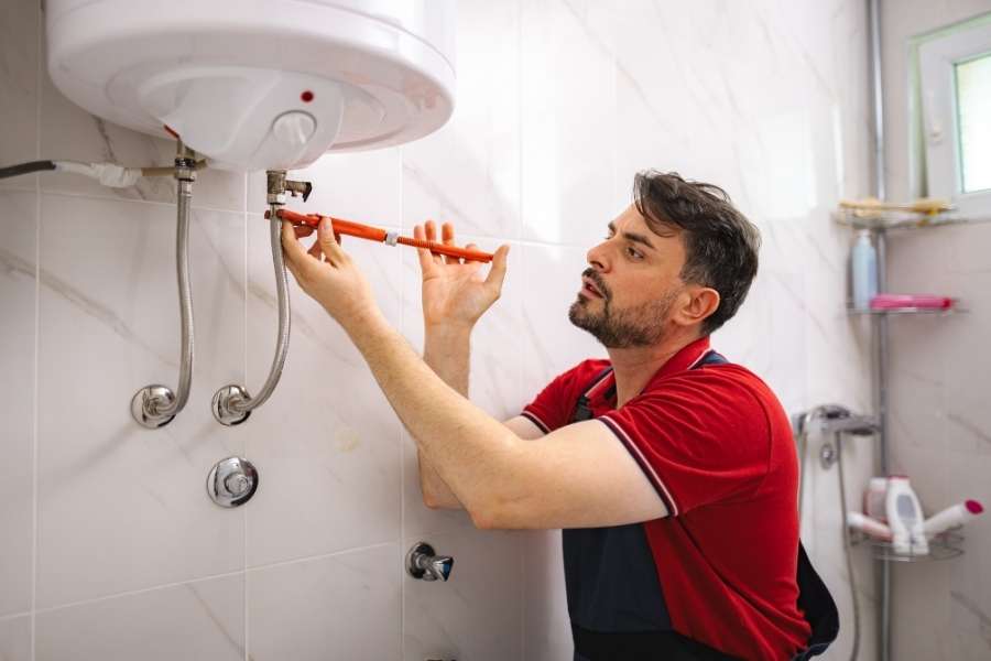 Un professionnel répare un chauffe-eau électrique fixé au mur d'une salle de bains.