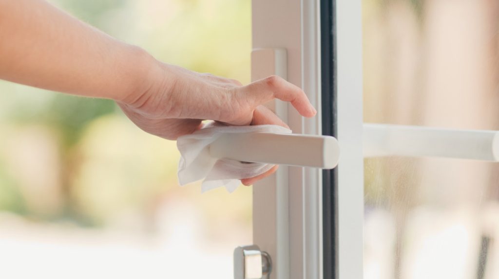 Gros plan d'une main nettoyant la poignée d'une fenêtre en PVC blanc avec une lingette, illustrant une étape clé pour savoir comment nettoyer menuiserie pvc jaunie.