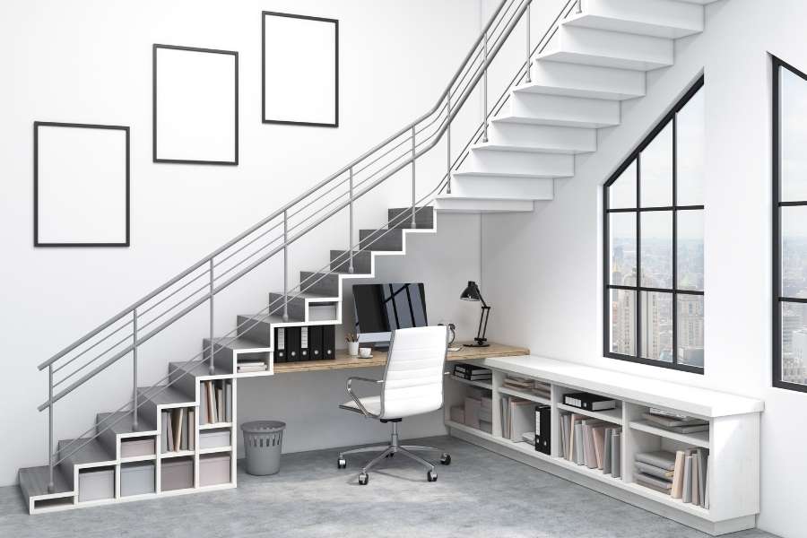 Un bureau à domicile moderne et lumineux avec une bibliothèque sur mesure intégrée sous un escalier design
