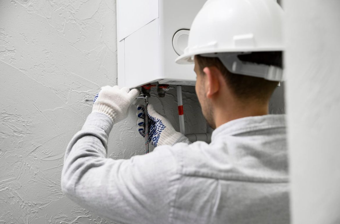 Un chauffagiste professionnel en casque de chantier effectue la révision chauffage avant hiver sur une chaudière.